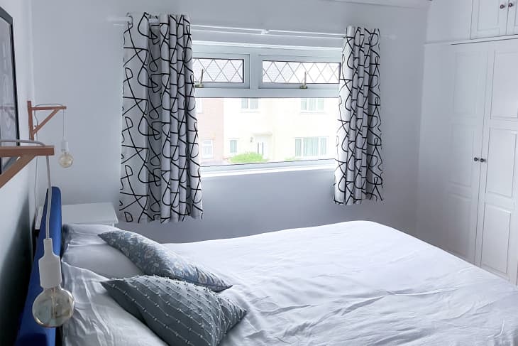 Neatly made bed in white painted bedroom with black and white graphic curtains.