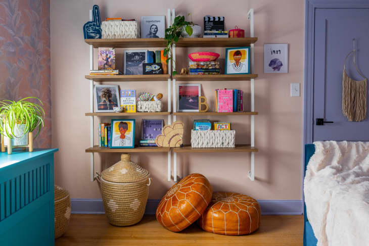 floating wood shelves with lots of colorful art and books, purple door, pink walls, orange floor cushions
