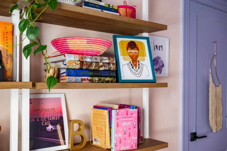 floating wood shelves with lots of colorful art and books, purple door, and pink walls.