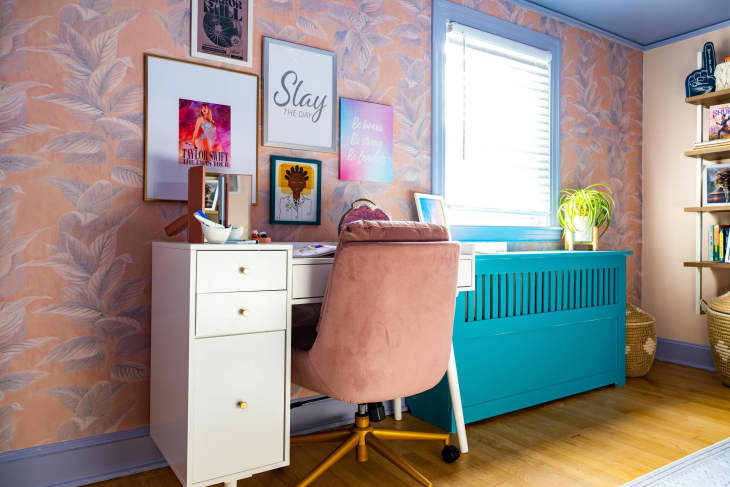 soft pink and purple floral wallpaper, purple trim, teal radiator cover, and white desk with pink swivel chair