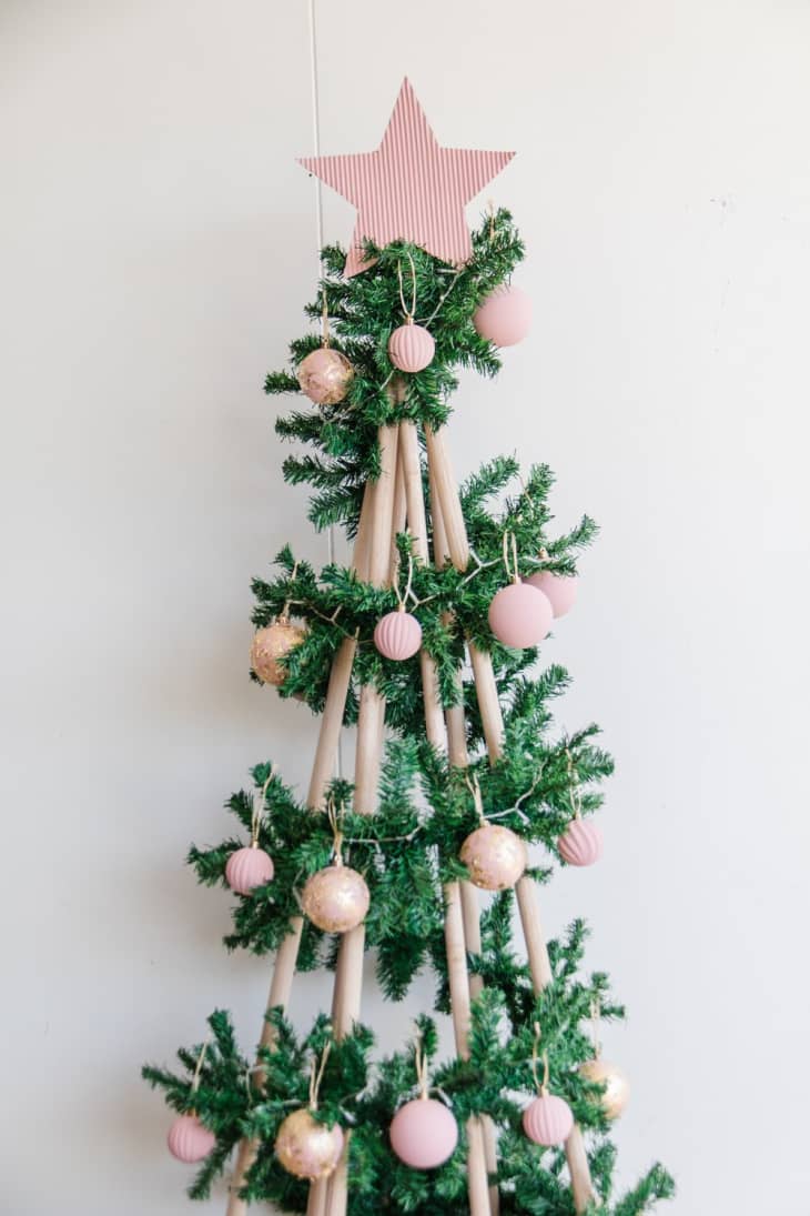 Christmas tree made with dowels wrapped in faux evergreen garland, and covered with round wood ornaments painted gold and pink.