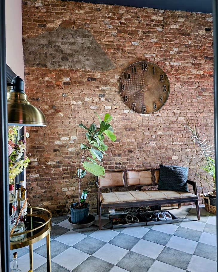 Large clock hangs on wall on brick lined entryway.