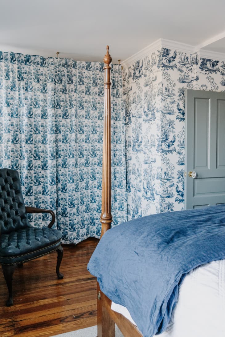 Blue toile wallpaper with dark wood floors and wood four poster bed, blue leather chair in corner and blue painted door