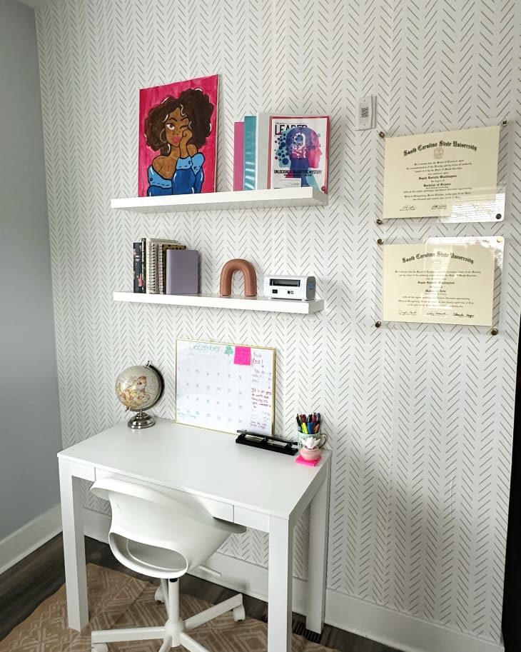 Office area with white wallpaper with black pattern, white desk and chair, and white floating shelves