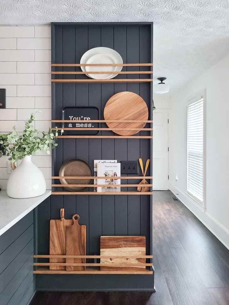 wood and gray open shelving/plate rack next to kitchen counter holding cutting boards, etc
