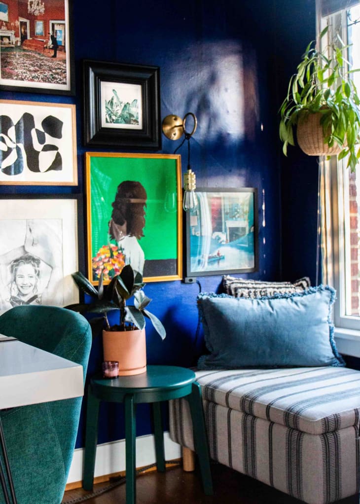A blue-walled office space with hanging plants, framed art work and a fabric love seat.