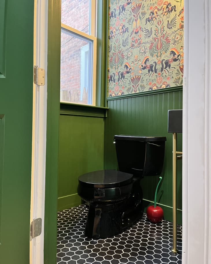 bathroom with green wainscoting, colorful horse-patterned wallpaper, gold accents, and black and white tile floor after makeover