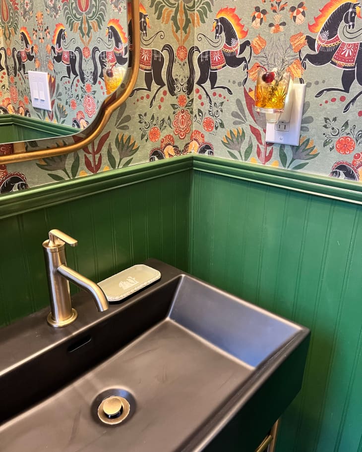 bathroom sink area with green wainscoting, horse wallpaper, large basin sink, and gold mirror after makeover