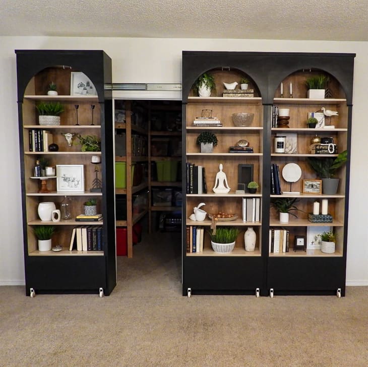 Black painted Ikea Billy bookcase filled with books and other objects opened to show storage space behind.