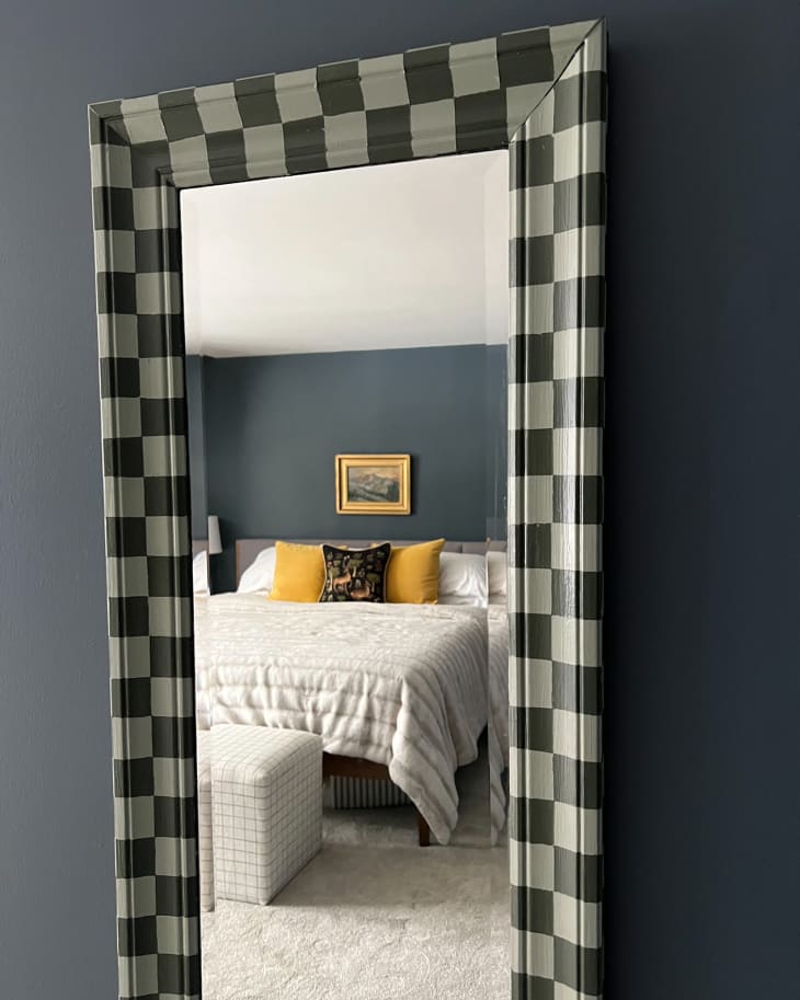 full length mirror with dark and light green checkered frame mounted on gray wall and reflection of bedroom