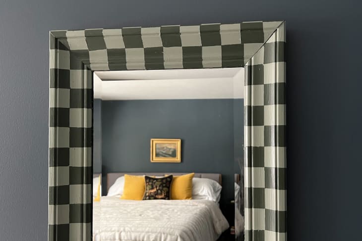 full length mirror with dark and light green checkered frame mounted on gray wall--detail of top of mirror