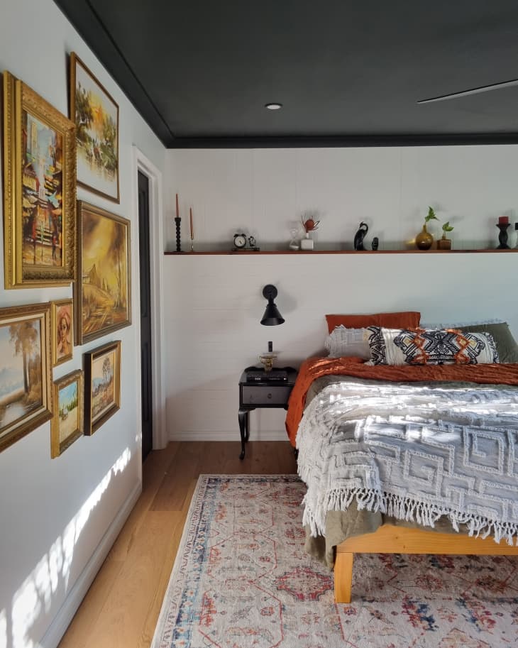white bedroom with black ceiling, gallery wall, and floating shelves above bed after makeover