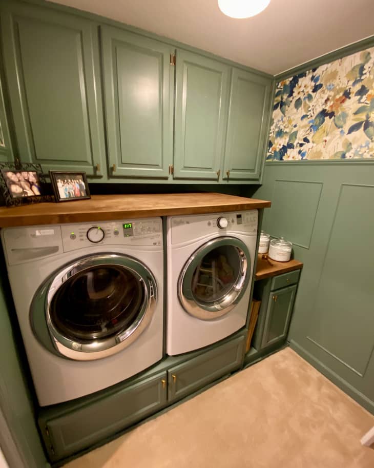 Green wainscoting, bold floral wallpaper on upper half of wall, countertop built on top of washer and dryer with built in cabinets above