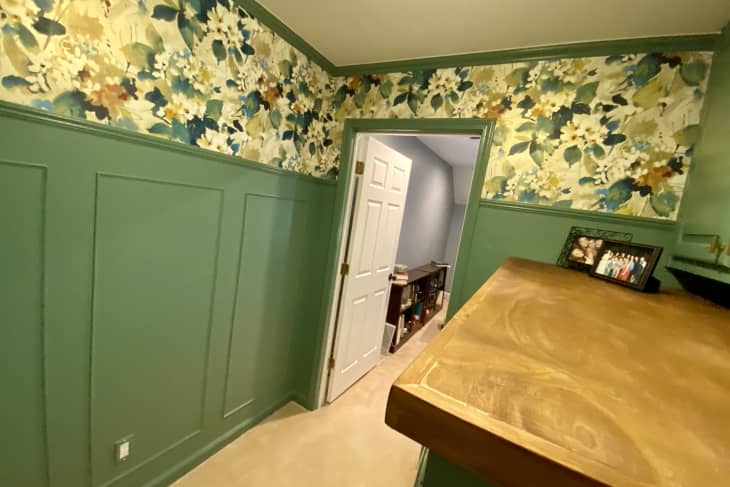 Green wainscoting, bold floral wallpaper on upper half of wall, countertop built on top of washer and dryer with built in cabinets above