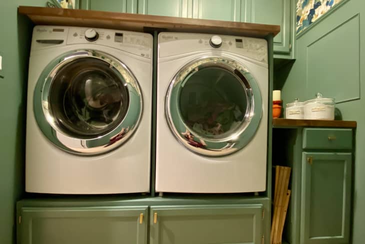 Washer and dryer built in to green cabinetry with wood countertop on top and drawers underneath