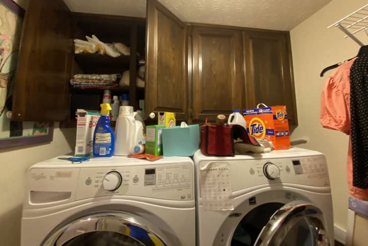 Wood cabinets with washer and dryer below, messy top with detergent and cleaning supplies everywhere