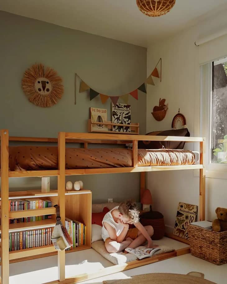 A child is reading on the floor under the lofted bunk bed.