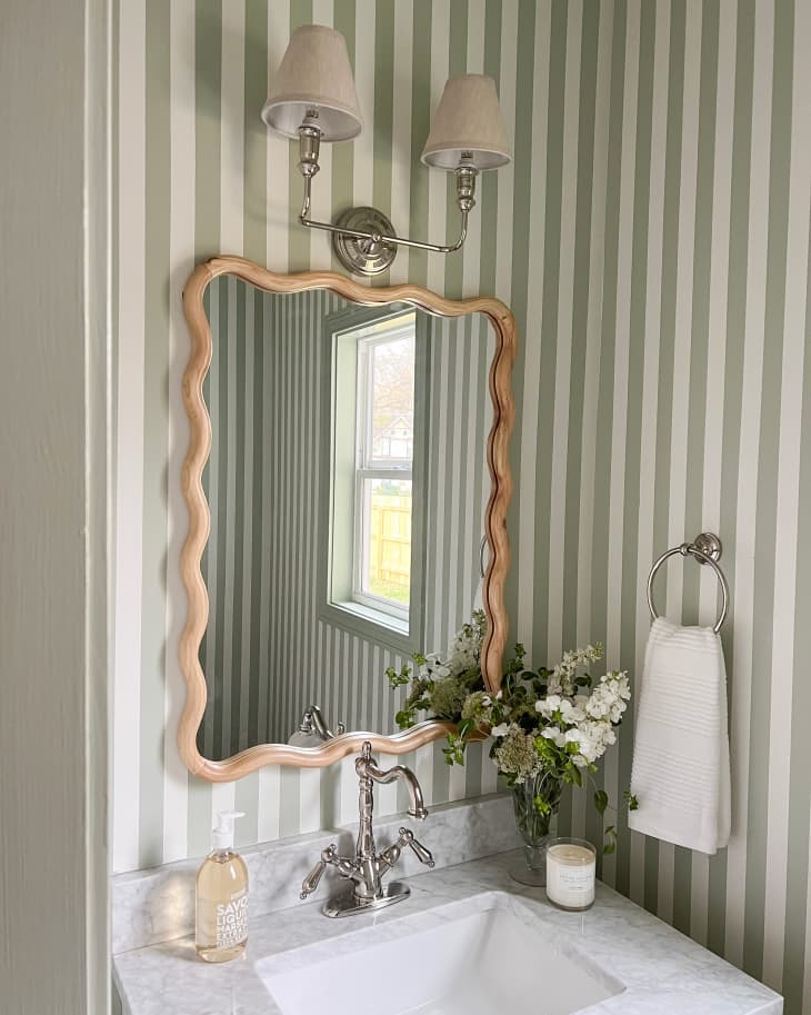 New mirror and lighting in wallpapered bathroom.