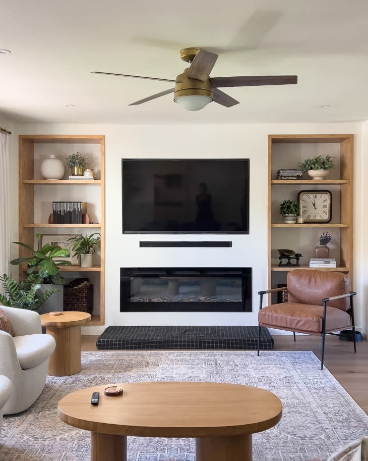 white living room with mounted TV with fireplace, wood shelves, plants, decor after remodel