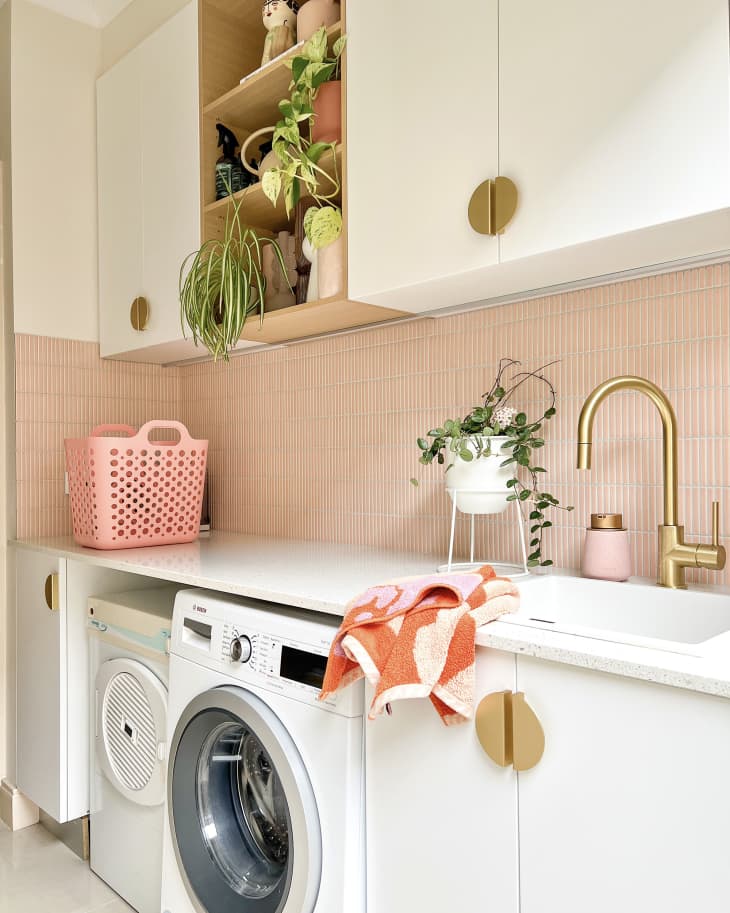 Laundry room with pink tiles, white cabinets with gold round pulls, and other gold details after renovation