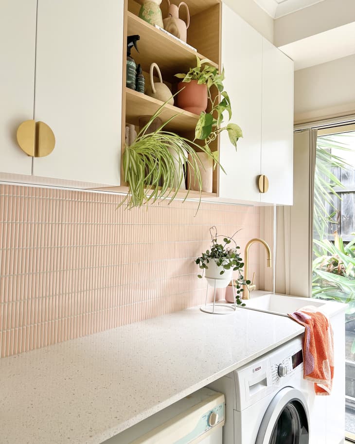 Laundry room with pink tiles, white cabinets with gold round pulls, and other gold details after renovation