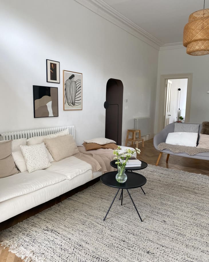Neutral art above light couch in living room with neutral rug, accent tables, and rattan light.