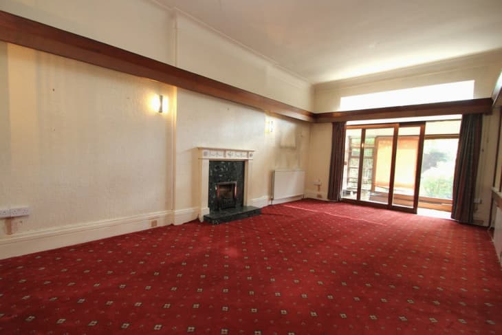 Empty living room with wood trim on walls, glass doors, and windows, dark marble fireplace, and red carpeting.