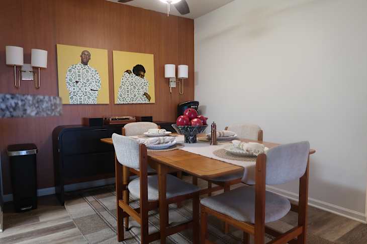 Dining area featuring a wooden table set with plates, a bowl of red apples, and two colorful wall art pieces.
