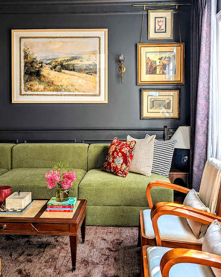 Cozy living room featuring a green sectional sofa with patterned pillows, a wooden coffee table, and framed artwork on dark walls.