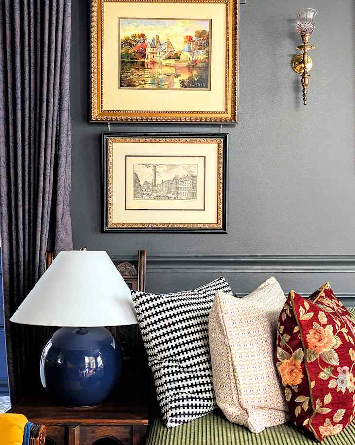 Cozy seating area featuring a blue lamp, patterned pillows, and framed artwork on a dark wall.