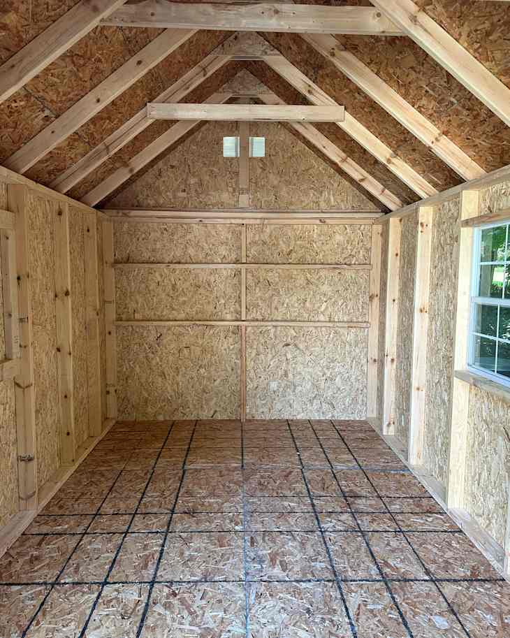 Interior of a wooden shed with exposed OSB walls, a peaked roof, and a grid-patterned floor.