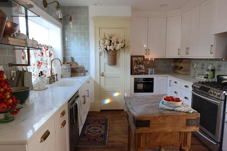 Bright kitchen featuring white cabinets, a wooden island, floral curtains, and a bowl of fresh tomatoes.