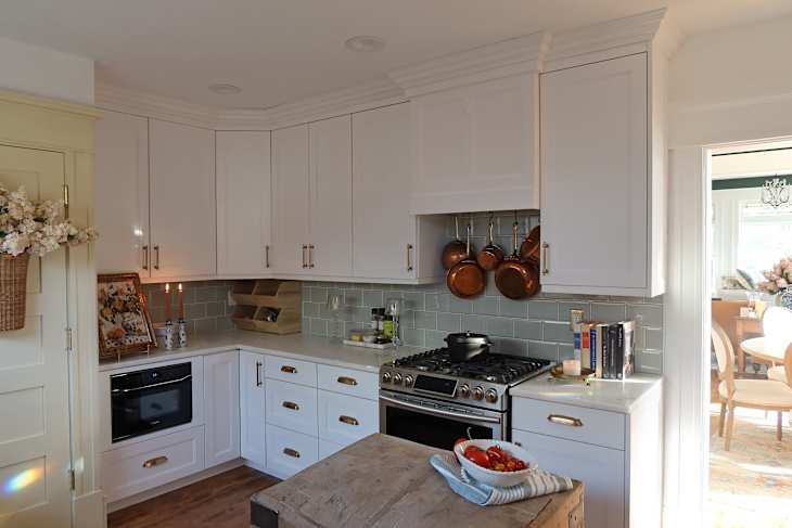 Bright kitchen with white cabinets, copper pots hanging, a wooden island, and a bowl of tomatoes on the counter.