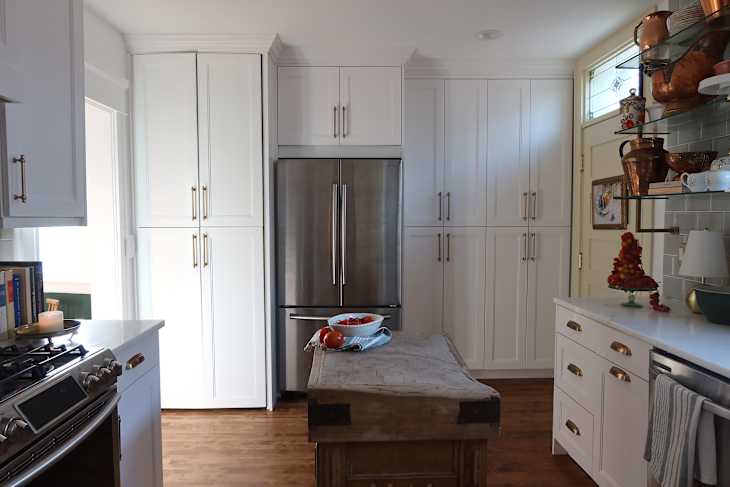 Modern kitchen with white cabinetry, stainless steel refrigerator, wooden island, and a bowl of tomatoes on the counter.