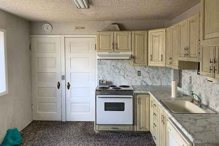 Kitchen with light wood cabinets, marble countertops, a white stove, and a sink, featuring a clock and double doors.