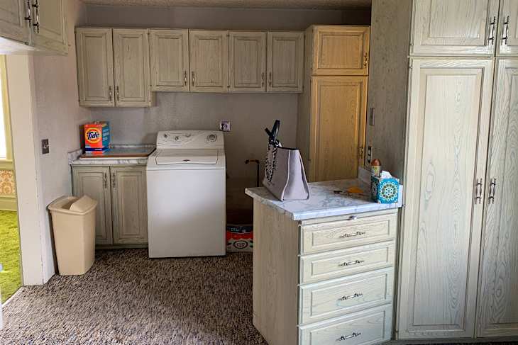 Laundry area with a washing machine, light wood cabinets, a marble countertop, and a bag on the counter.