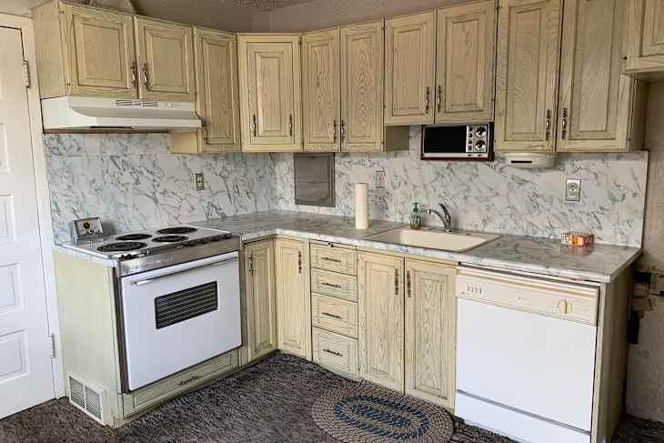 Compact kitchen with light wood cabinets, marble countertops, stove, sink, and a dishwasher.