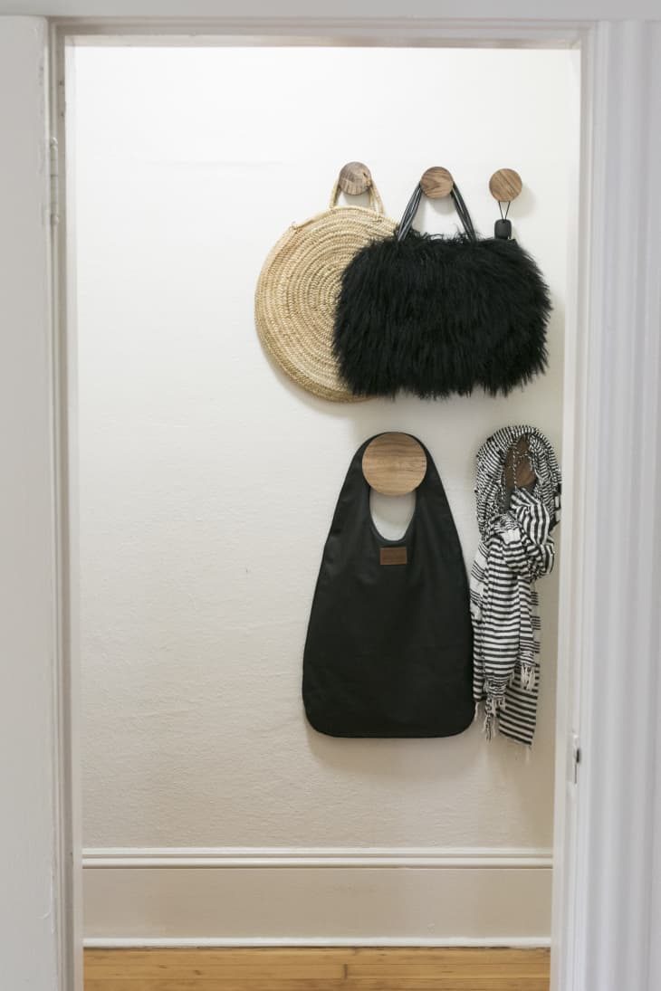 Fun purses hanging from round wooden hooks in a small apartment entryway