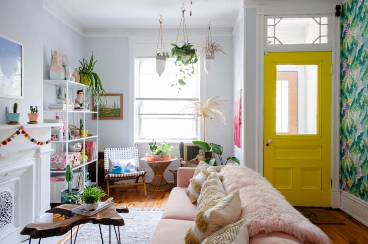 An entryway opening into a living room with whimsical decor, plants, and a bright yellow entry door