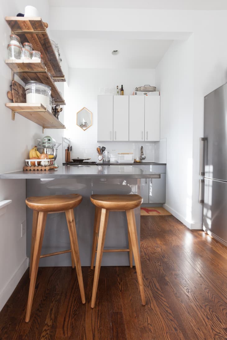 Two wood stools under the counter of a grey kitchen island in an organic modern apartment kitchen