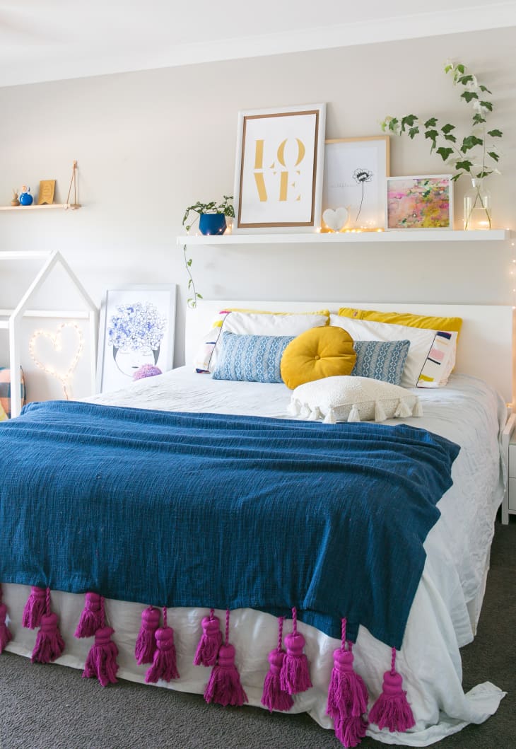 A floating shelf with hanging art above a colorful bed