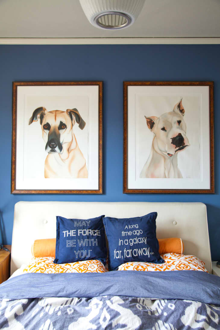 A bedroom with blue walls and two dog portraits above the bed.