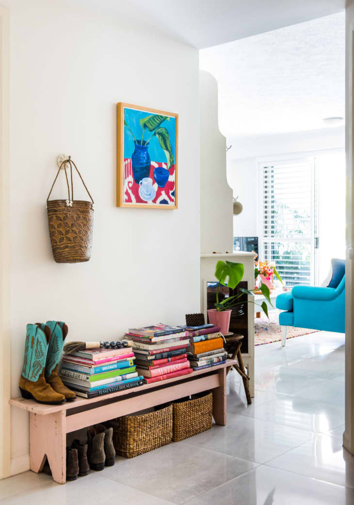 A bright entryway with a bench covered with stacks of books, baskets are underneath