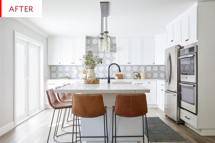 A bright white kitchen with a light blue mosaic tile backsplash, stainless steel appliances, and camel leather stools around the island