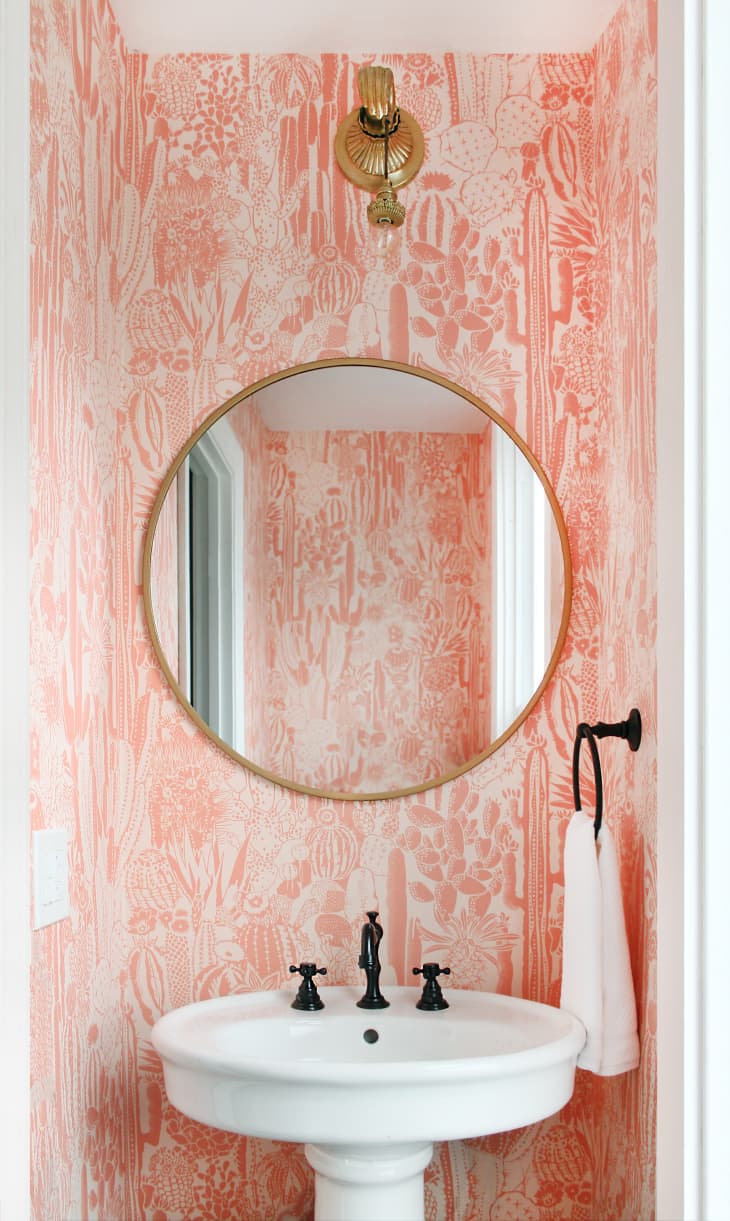 Powder room with pink cactus wallpaper and gold round mirror