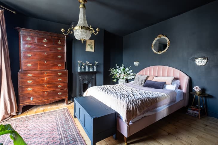 A bedroom painted in matte dark blue with a light pink bed, bedding and curtains.
