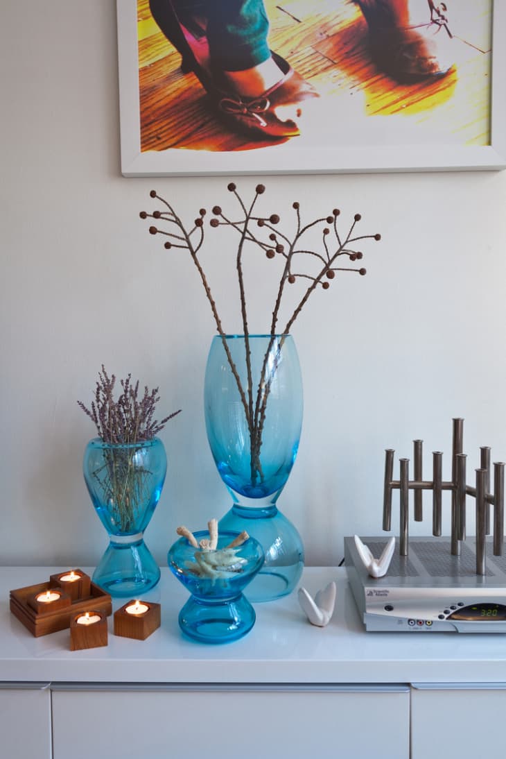 Three blue glass vases filled with dry flowers on top of a white modern cabinet
