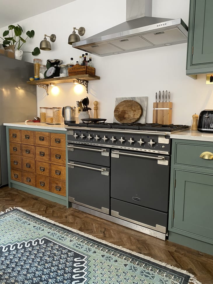 This colorful UK home features a modern kitchen addition that seamlessly blends traditional and contemporary design elements. The apothecary kitchen boasts a stylish mix of open shelving, sleek countertops, and vibrant pops of color, creating a unique and inviting space for cooking and entertaining.
