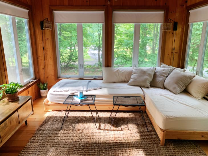Wood wall sun room with lots of windows over looking forest, with a white daybed sectional sofa
