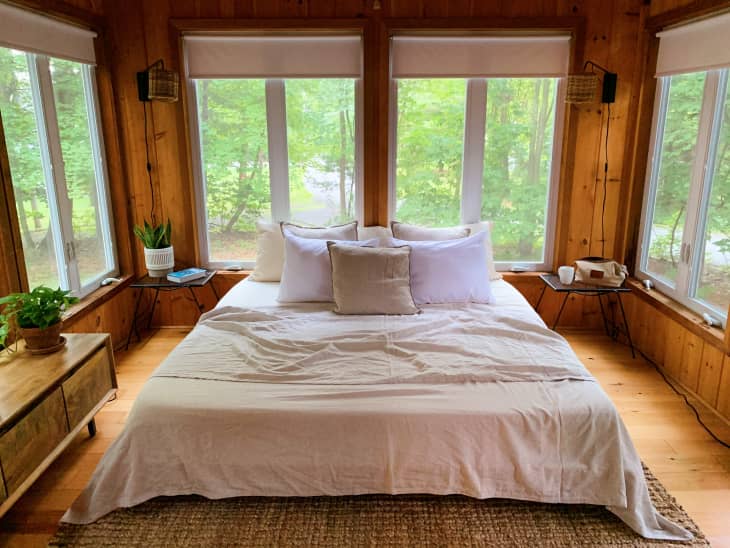 Cabin guest bedroom with wood walls, a king-sized bed, and lots of windows overlooking a forest
